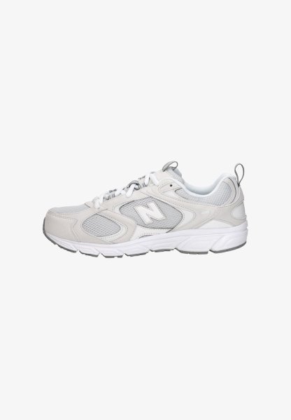 Zapatilla deportiva blanca y gris con paneles de malla, cierre de cordones, suela acolchada y tiradores en la lengüeta y el talón.