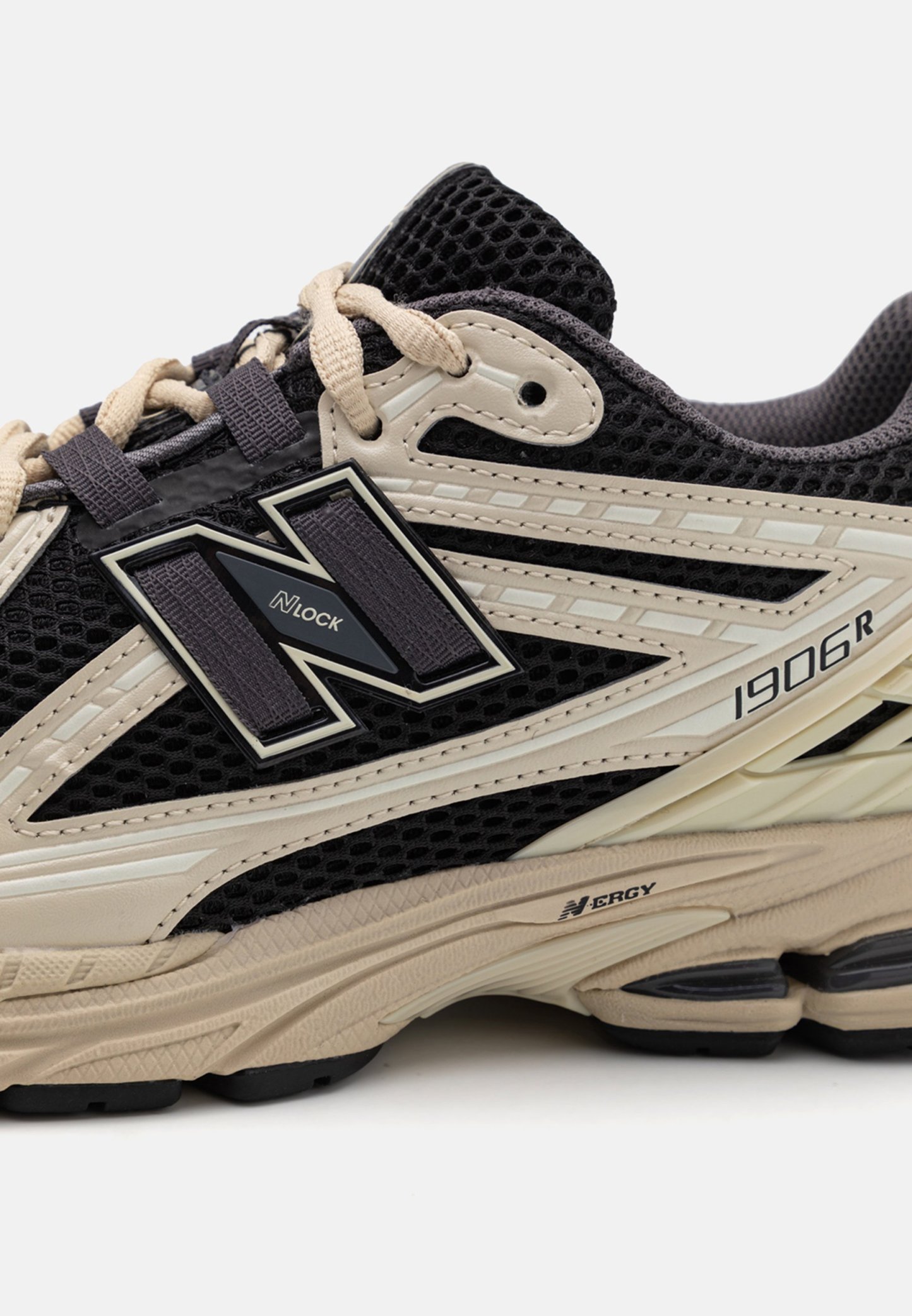 Zapatilla New Balance 1906R negra y beige con parte superior de malla, cordones beige, logotipo N Lock y detalle de suela acolchada Enerzy.