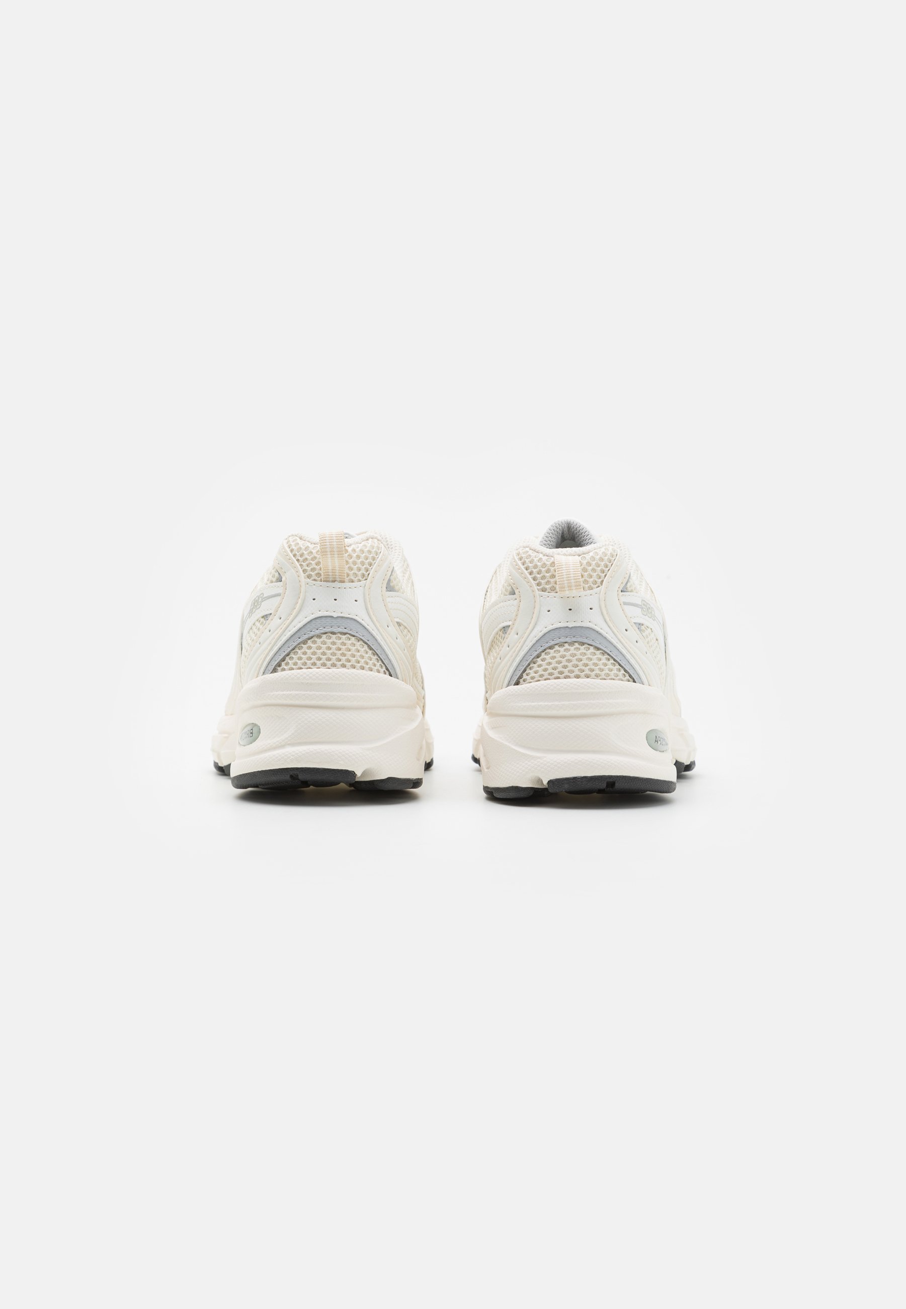 Par de zapatillas para correr confeccionadas con malla sintética de color blanco hueso, vistas desde atrás, sobre un fondo blanco liso.
