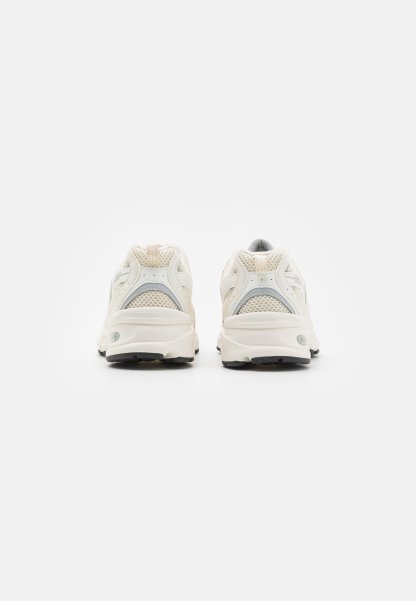 Par de zapatillas para correr confeccionadas con malla sintética de color blanco hueso, vistas desde atrás, sobre un fondo blanco liso.