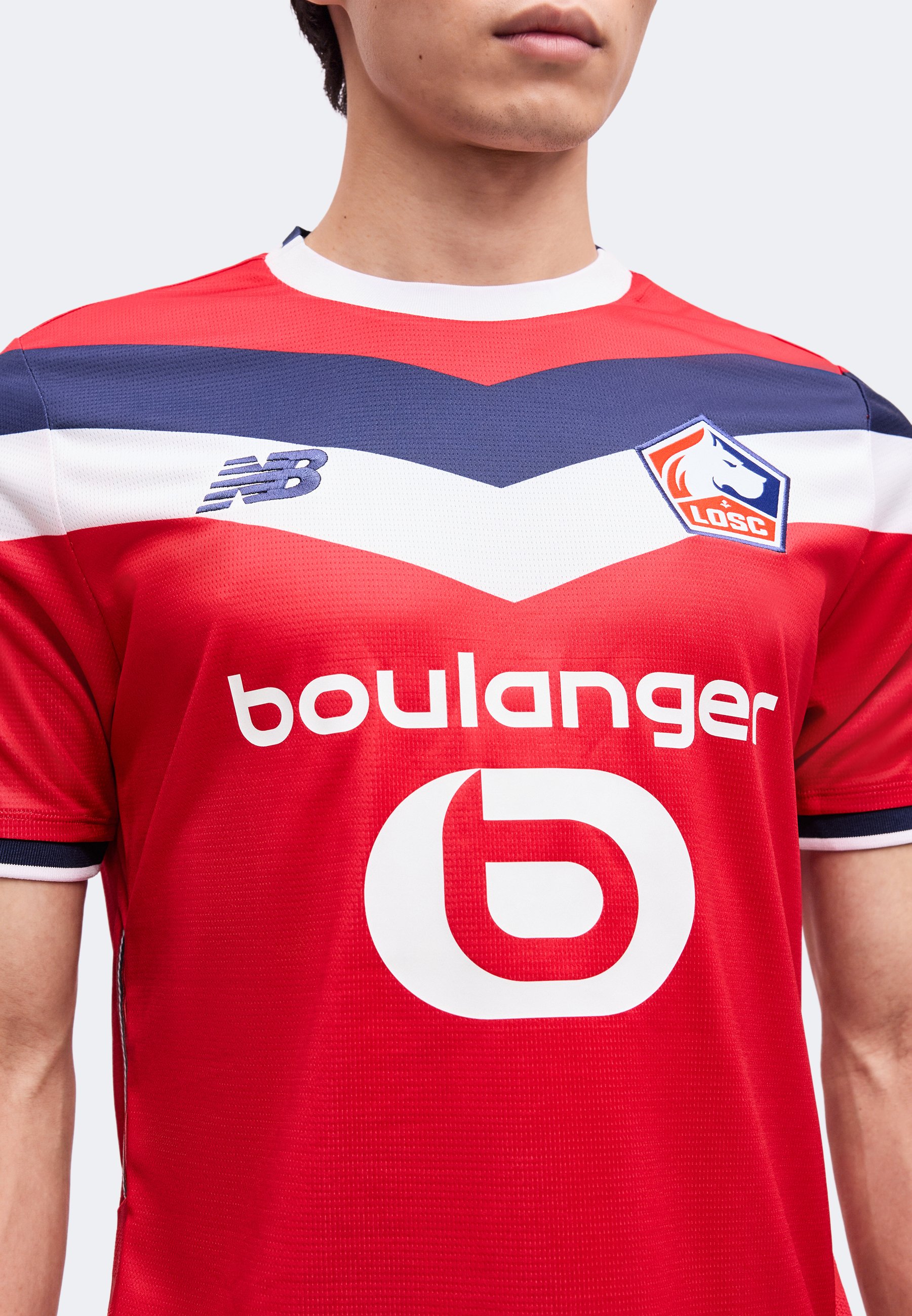 Hombre que lleva una camiseta de fútbol del LOSC Lille en rojo, blanco y azul con el logo de New Balance y el patrocinador Boulanger en el frente.