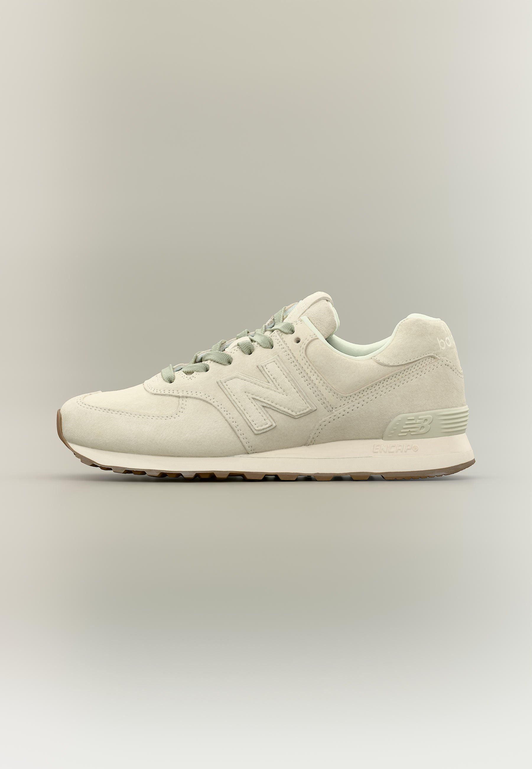 Zapatilla New Balance beige claro con textura de ante, cordones y suela acolchada, mostrada de lado sobre un fondo neutro.