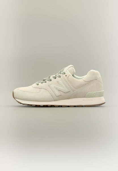 Zapatilla New Balance beige claro con textura de ante, cordones y suela acolchada, mostrada de lado sobre un fondo neutro.