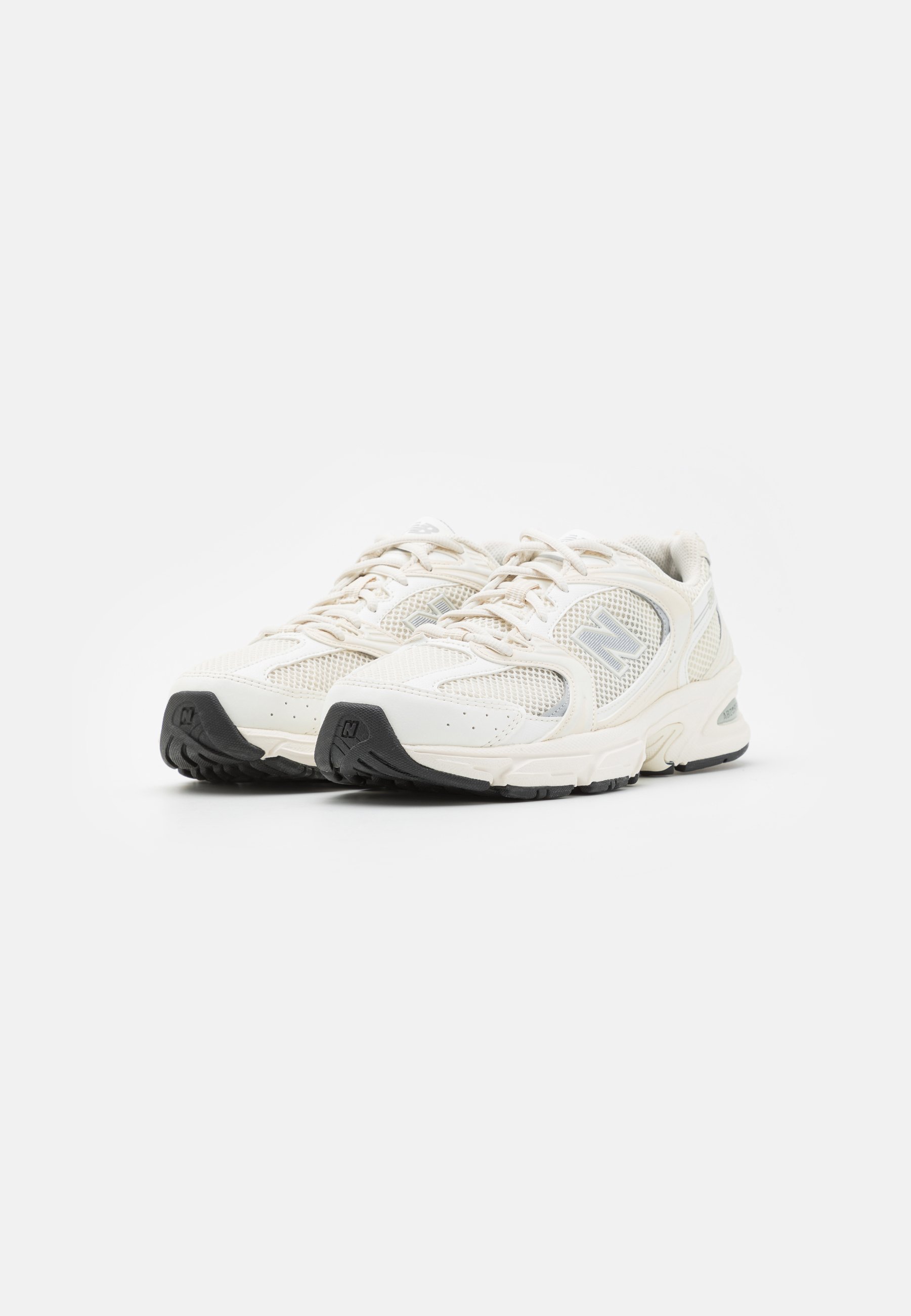 Par de zapatillas deportivas de color blanco roto con paneles de malla y suelas de goma negras sobre fondo blanco.