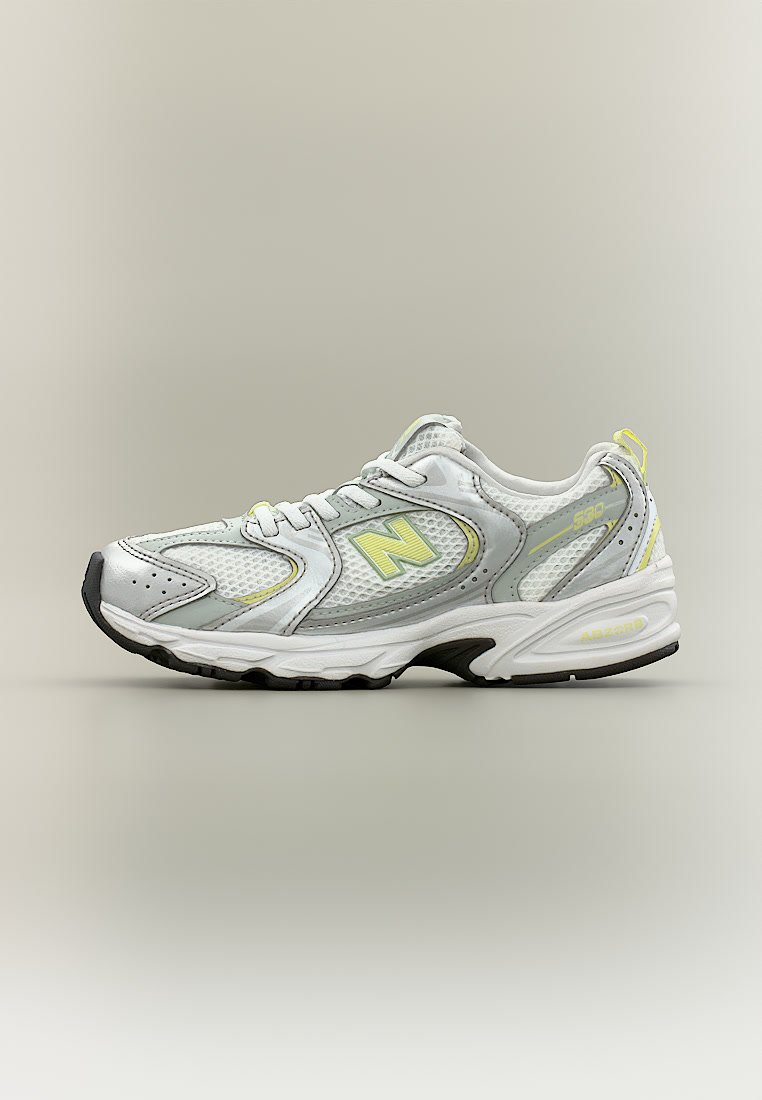 Zapatilla deportiva blanca y gris con detalles amarillos, paneles de malla, cierre de cordones y suela negra, posicionada de perfil sobre un fondo sencillo.