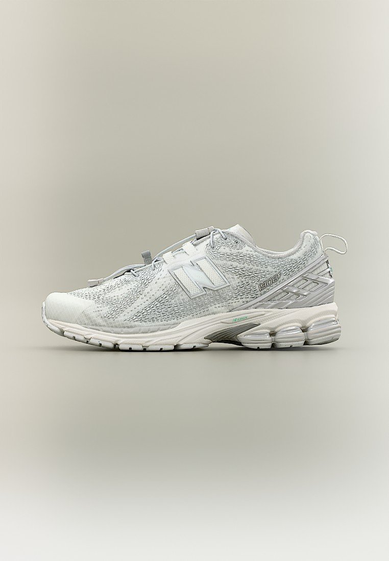 Zapatilla deportiva New Balance blanca con parte superior texturizada, suela acolchada y tira para tirar en el talón, mostrada de perfil sobre un fondo neutro.
