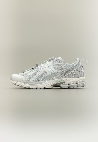 Zapatilla deportiva New Balance blanca con parte superior texturizada, suela acolchada y tira para tirar en el talón, mostrada de perfil sobre un fondo neutro.