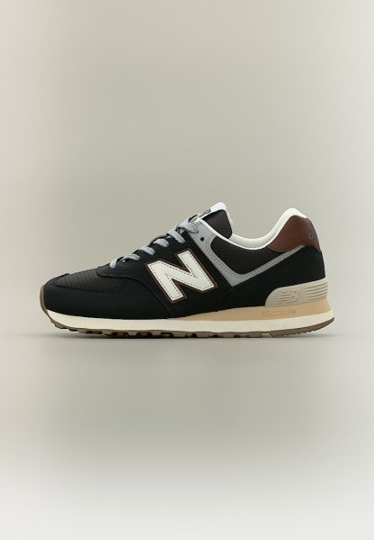 Zapatilla New Balance negra, gris y marrón con logo "N" blanco, entresuela beige y suela exterior texturizada, mostrada de perfil sobre un fondo neutro.