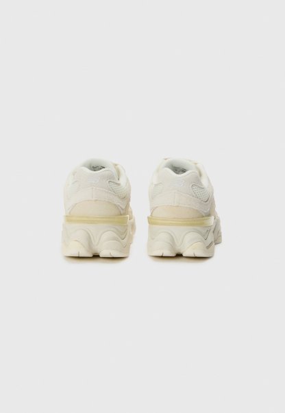 Par de zapatillas de color blanco roto con suelas gruesas, vistas desde atrás sobre un fondo liso gris claro.