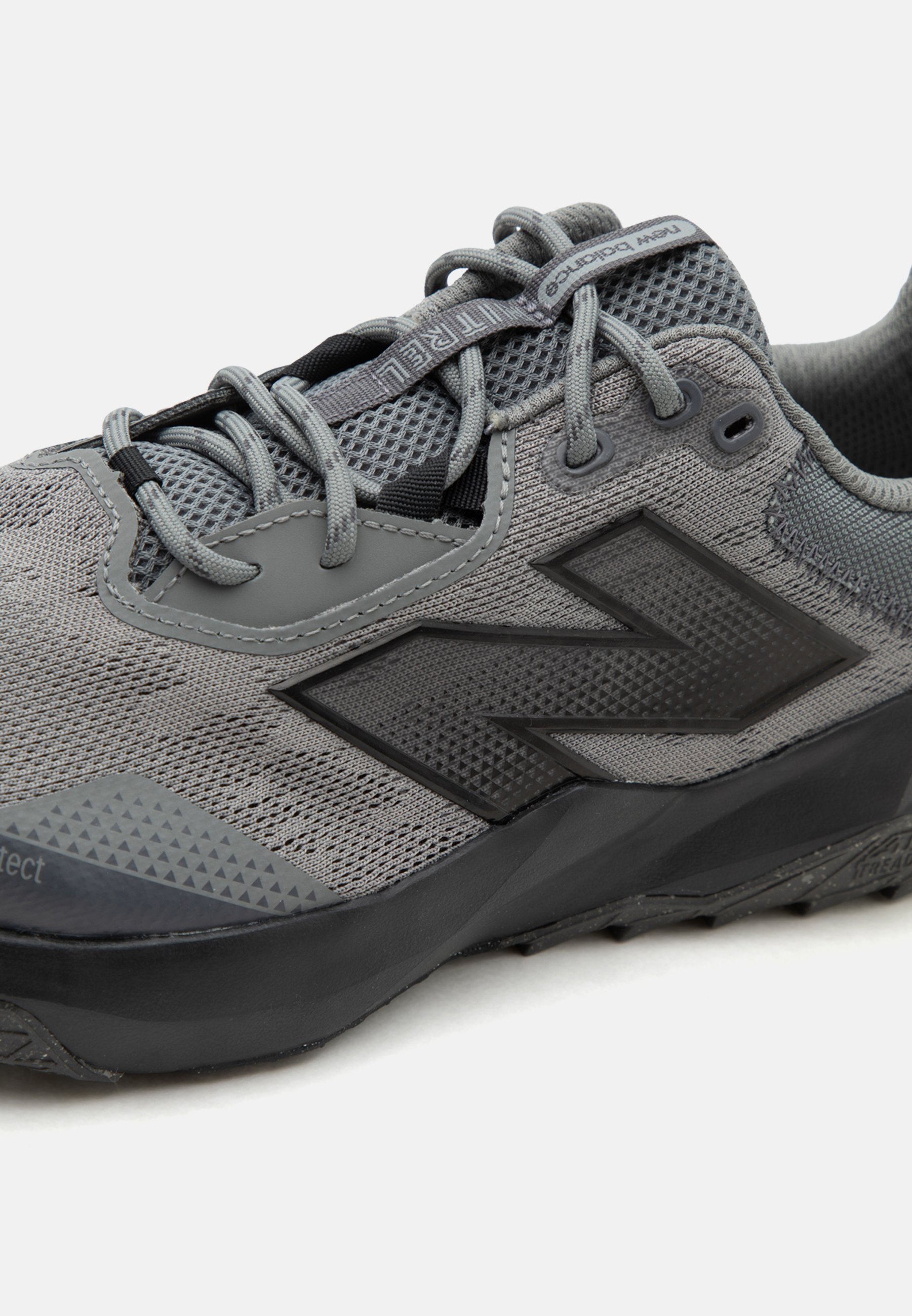 Zapatilla deportiva gris New Balance con parte superior de malla, suela negra y logo reflectante, con cordones grises y cuello acolchado.