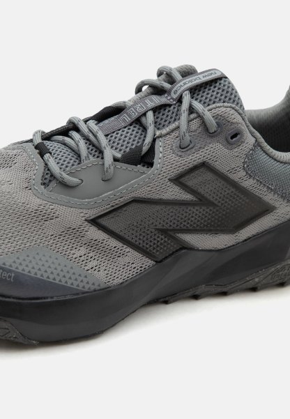 Zapatilla deportiva gris New Balance con parte superior de malla, suela negra y logo reflectante, con cordones grises y cuello acolchado.