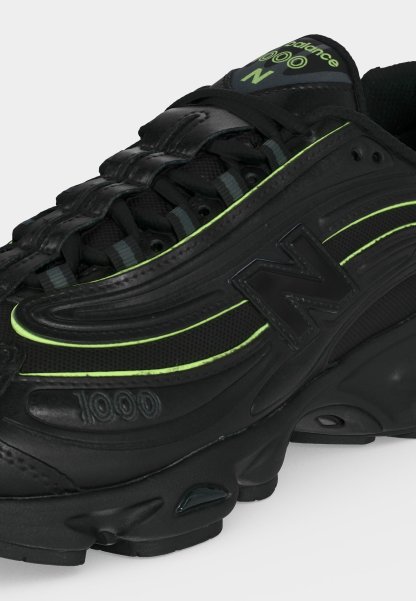 Zapatilla negra New Balance 1000 con acentos en verde neón, materiales de malla y cuero, cierre con cordones y suela gruesa acolchada.
