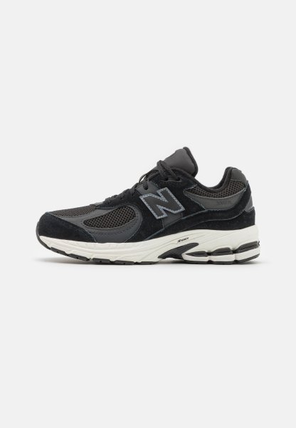 Zapatilla negra con parte superior de malla y ante, que presenta una entresuela blanca, acentos grises y una suela texturizada para agarre y comodidad.