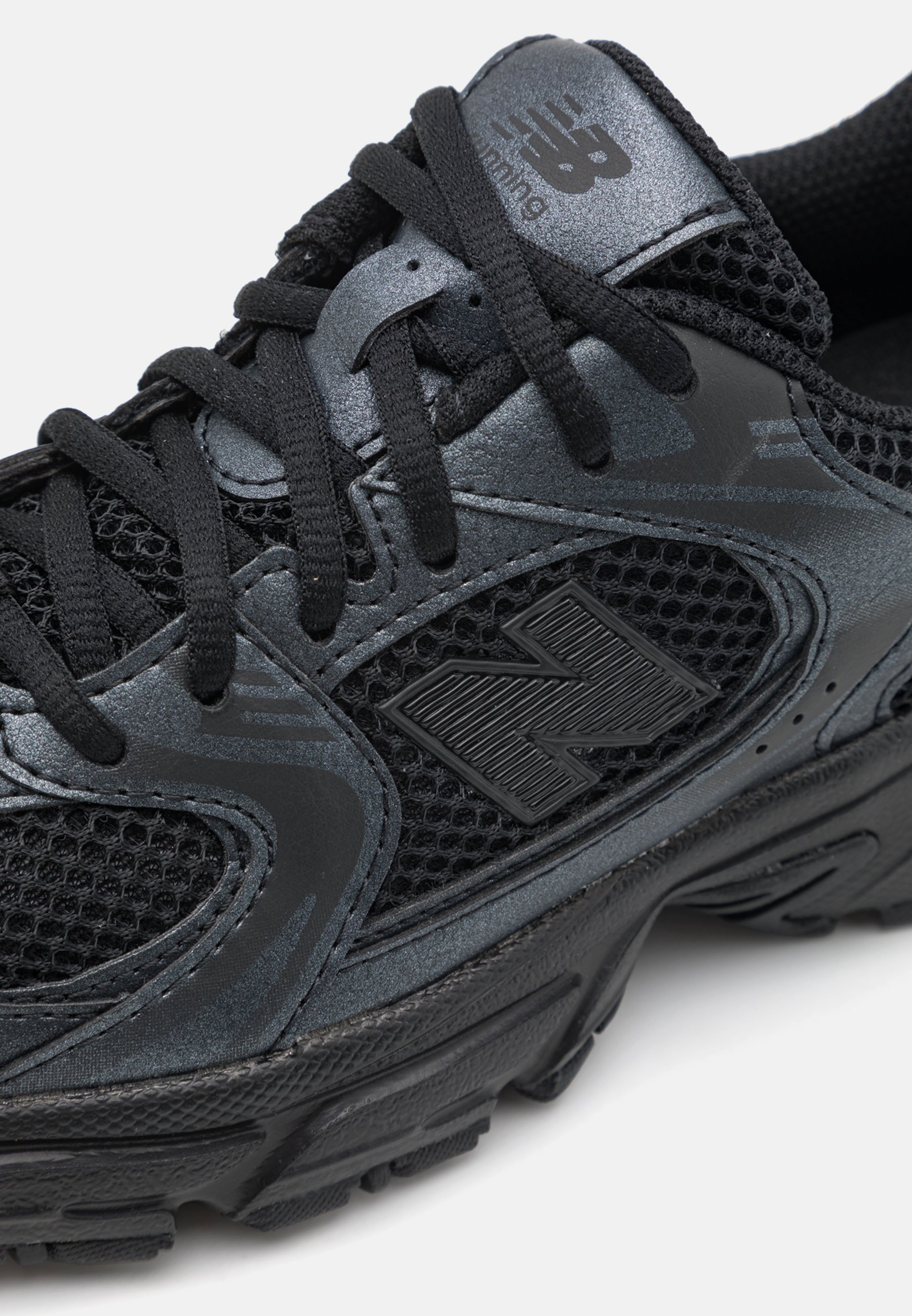 Zapatilla deportiva negra con parte superior de malla, acentos sintéticos texturizados y una suela moldeada con un dibujo en la banda de rodadura para mayor tracción.