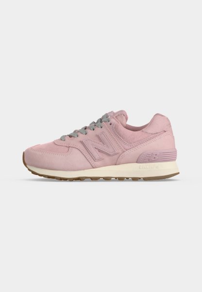 Zapatilla de ante rosa claro con cordones grises, entresuela blanca y suela exterior de goma marrón, con un "N" de marca en el lateral.