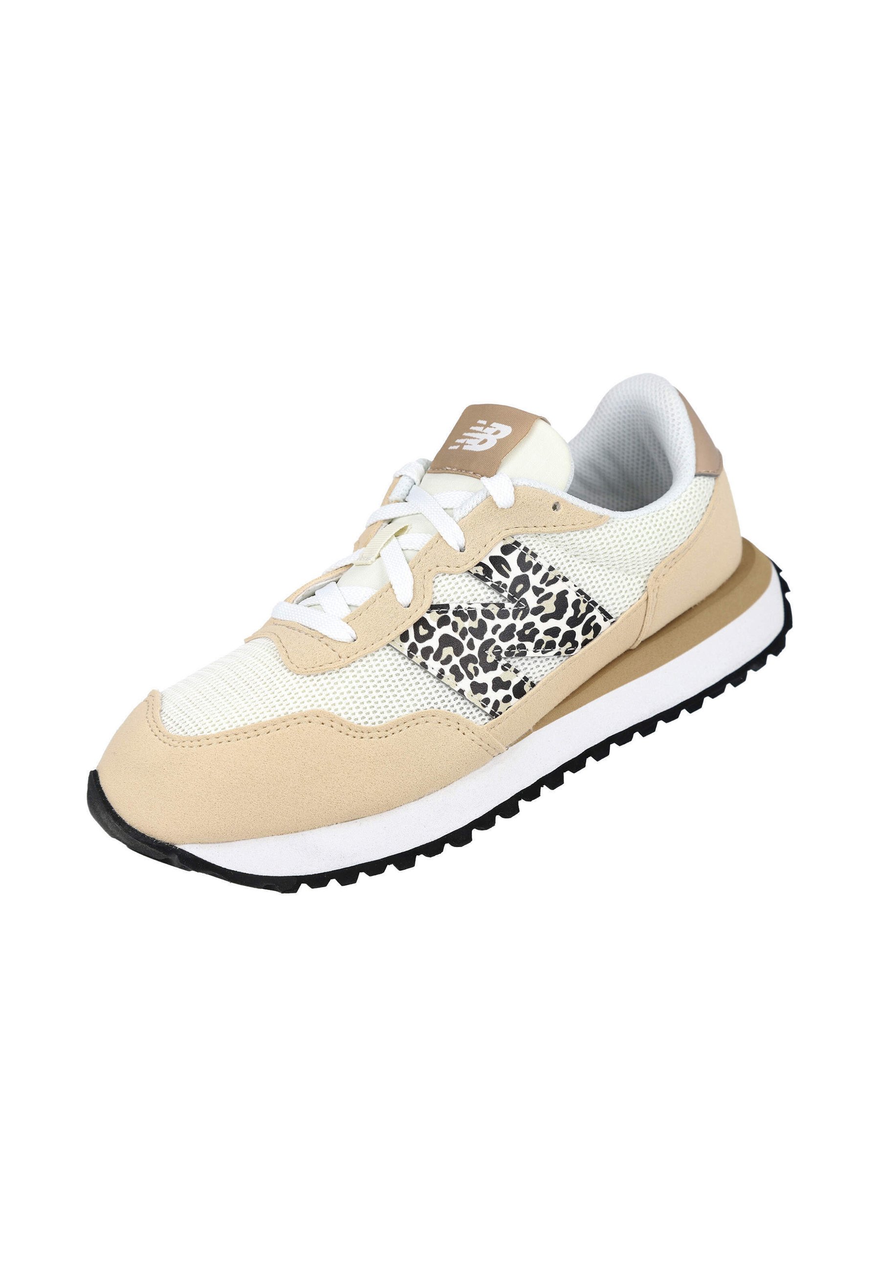 Zapatilla New Balance beige y blanca con cordones blancos, logo con estampado de leopardo en el lateral y suela negra texturizada, aislada sobre fondo blanco.