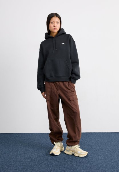 Sudadera negra con capucha y bolsillo frontal, combinada con pantalones cargo anchos marrones y zapatillas beige con acentos y cordones crema.