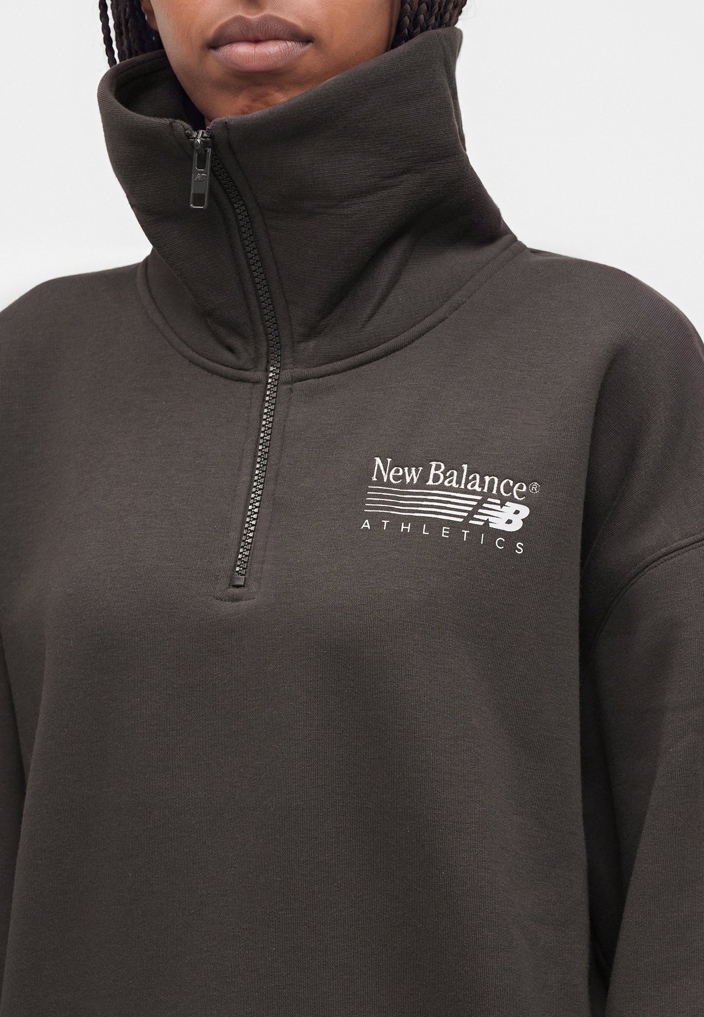 Persona que lleva un jersey oscuro de New Balance Athletics con cremallera de un cuarto y cuello alto, enfocándose en el torso superior y el logo.