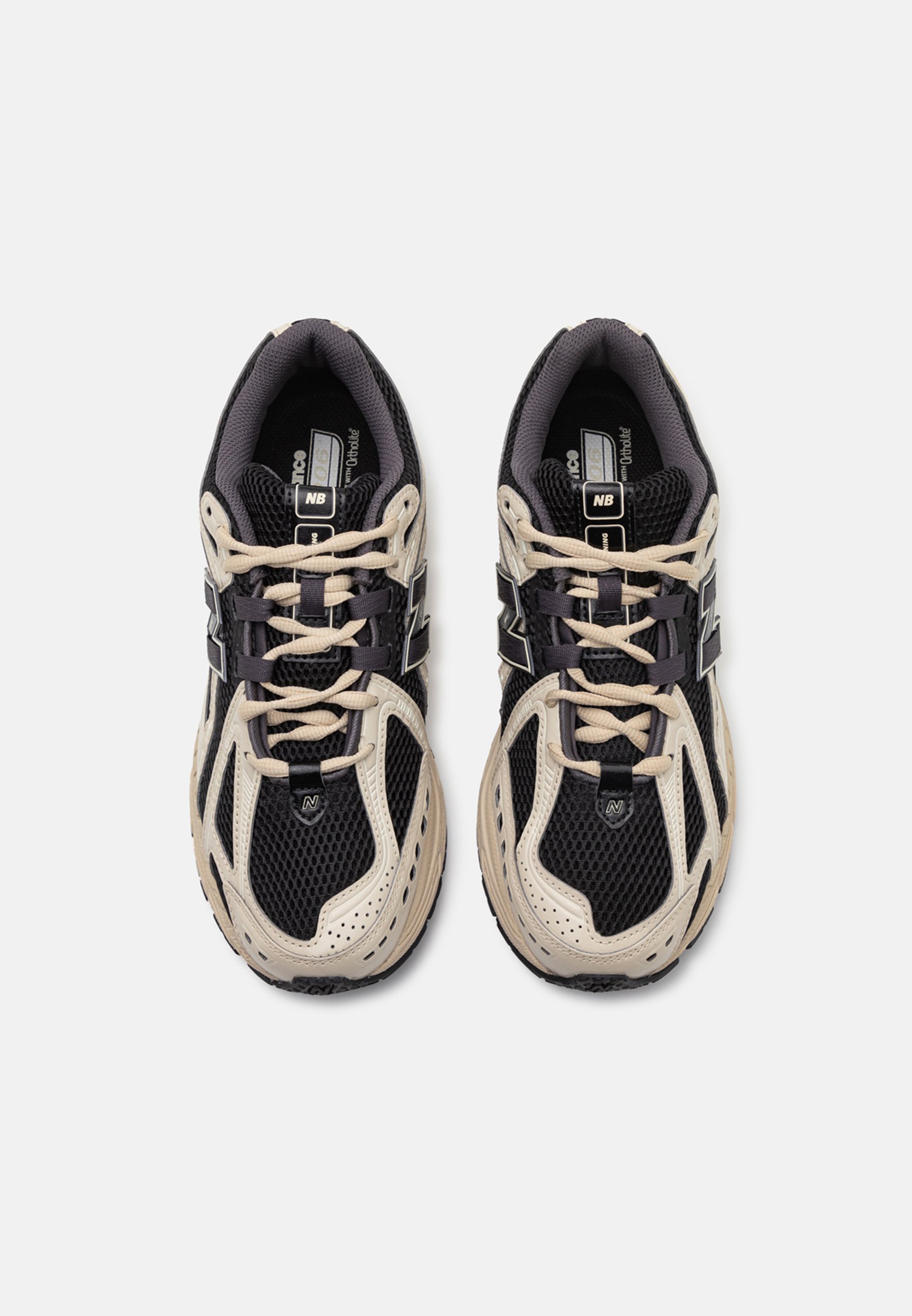 Par de zapatillas de correr New Balance en negro y beige con tela de malla y cordones, vistas desde arriba sobre un fondo blanco liso.