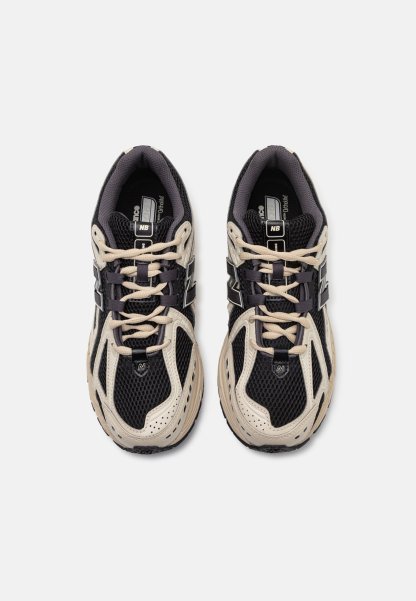 Par de zapatillas de correr New Balance en negro y beige con tela de malla y cordones, vistas desde arriba sobre un fondo blanco liso.