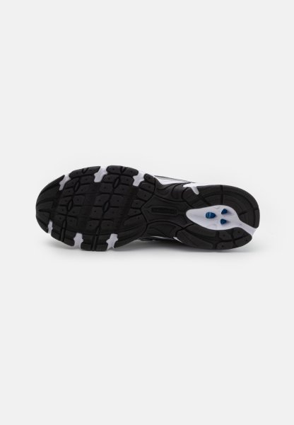 Suela de zapato deportivo en blanco y negro con goma texturizada para tracción, que presenta un logo y dos agujeros de acento en azul.
