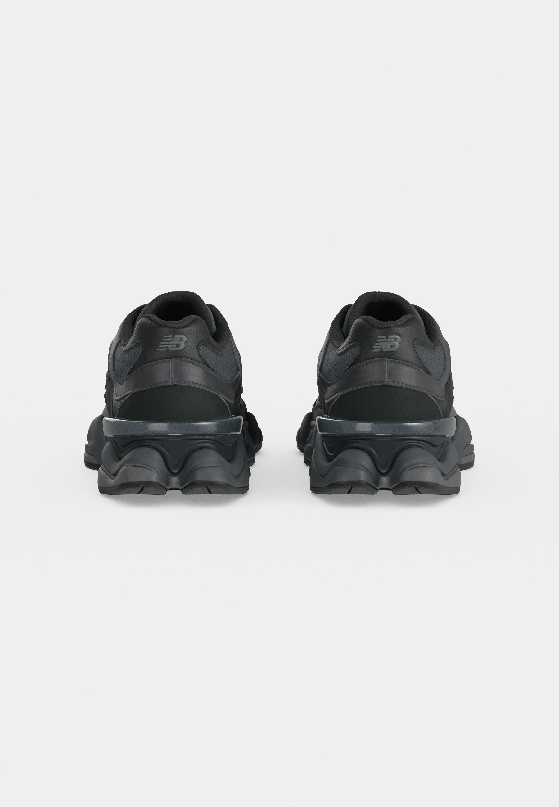 Par de zapatillas negras New Balance mostradas desde atrás sobre una superficie y fondo gris claro liso.