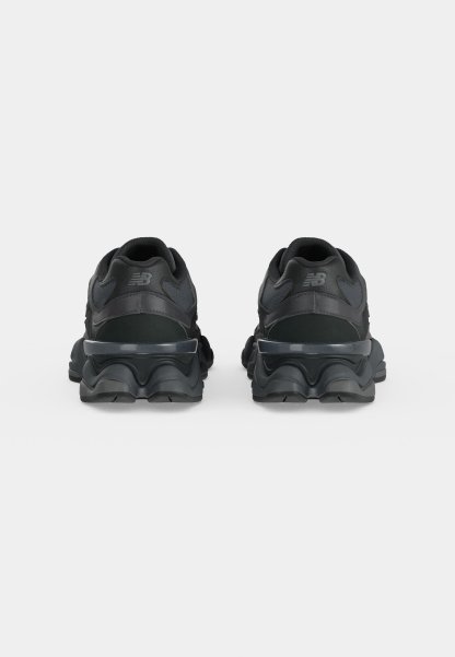 Par de zapatillas negras New Balance mostradas desde atrás sobre una superficie y fondo gris claro liso.