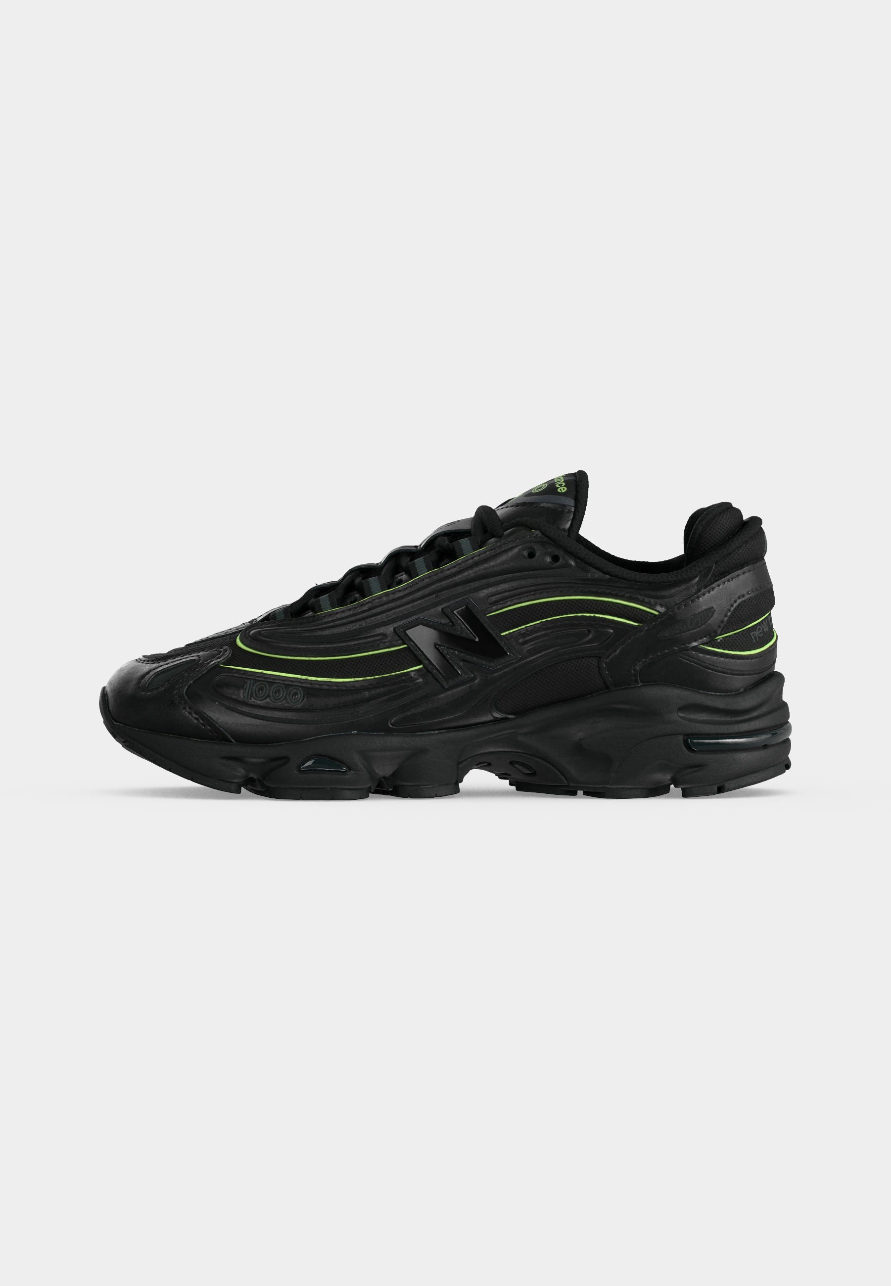 Zapatilla deportiva negra con detalles en verde neón, suela gruesa y logo "N" en el lateral, vista desde el lado exterior.