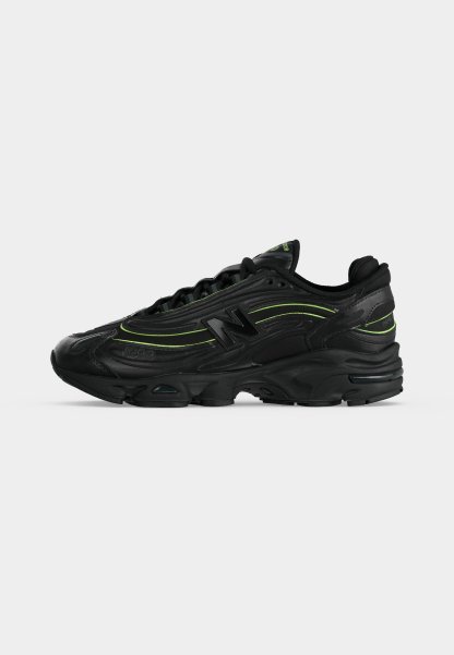 Zapatilla deportiva negra con detalles en verde neón, suela gruesa y logo "N" en el lateral, vista desde el lado exterior.