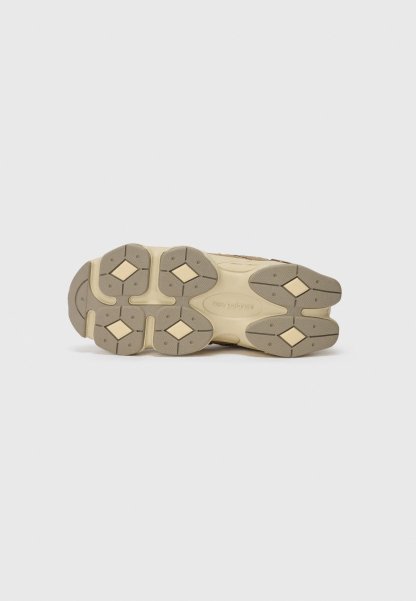 La suela de la zapatilla cuenta con un caucho duradero y texturizado en una combinación de colores beige y topo, con acentos en forma de diamante y un diseño antideslizante.