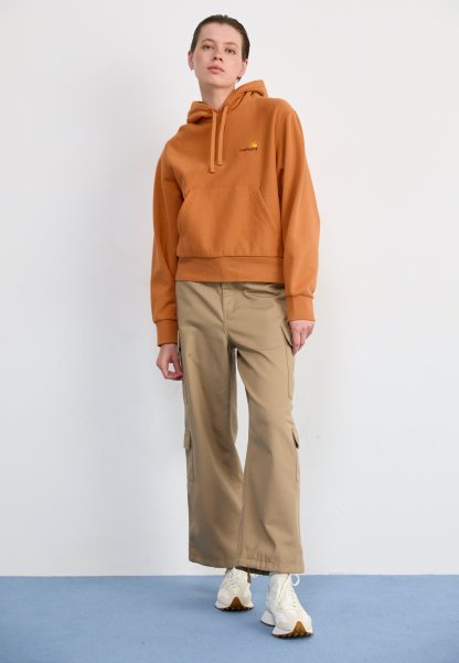Sudadera corta marrón con un bolsillo frontal y un pequeño logo, combinada con pantalones cargo beige de pierna ancha y zapatillas blancas.