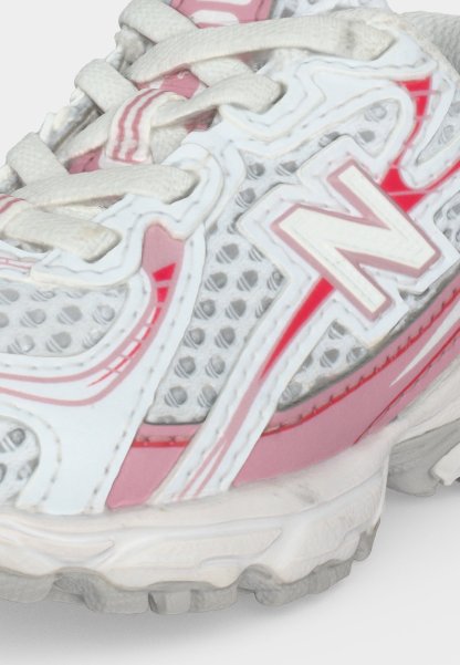 Zapatilla de running New Balance blanca y rosa con tejido de malla, cordones blancos y suela texturizada, mostrada en detalle en primer plano.