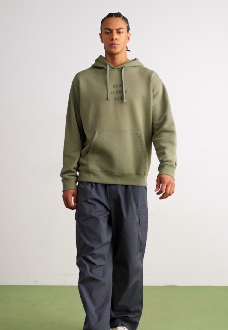 Sudadera verde oliva con bolsillo frontal y capucha con cordón, combinada con pantalones cargo gris oscuro que tienen bolsillos laterales.