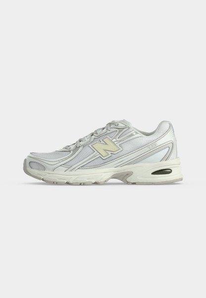 Zapatilla de running New Balance blanca y gris claro con parte superior de malla, cierre de cordones y suela acolchada gruesa sobre un fondo llano y claro.