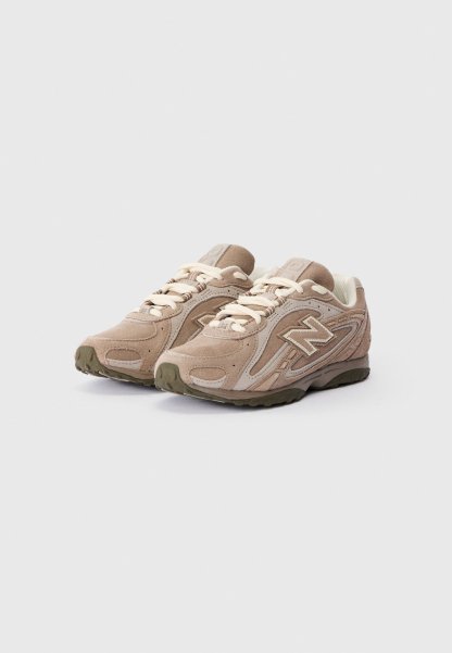 Un par de zapatillas New Balance de gamuza y malla beige con cordones blancos sobre un fondo gris claro liso.