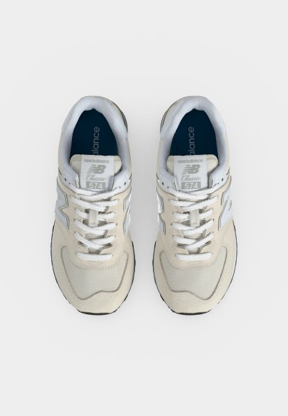 Par de zapatillas New Balance 574 Classic beige y blancas vistas desde arriba sobre un fondo claro.