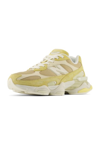 Zapatilla New Balance crema y amarilla con paneles de malla, cordones blancos y suela gruesa mostrada desde el frente sobre fondo blanco.