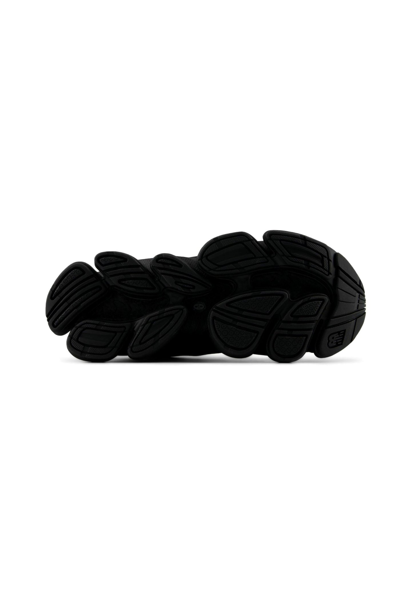 Suela de un zapato deportivo negro que muestra patrones segmentados de banda de rodadura de goma para agarre y flexibilidad sobre un fondo blanco.