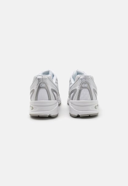Zapatillas deportivas blancas con parte superior de malla, acentos plateados, cuello acolchado y suela en contraste. Presenta una puntera redondeada y detalles de ventilación.