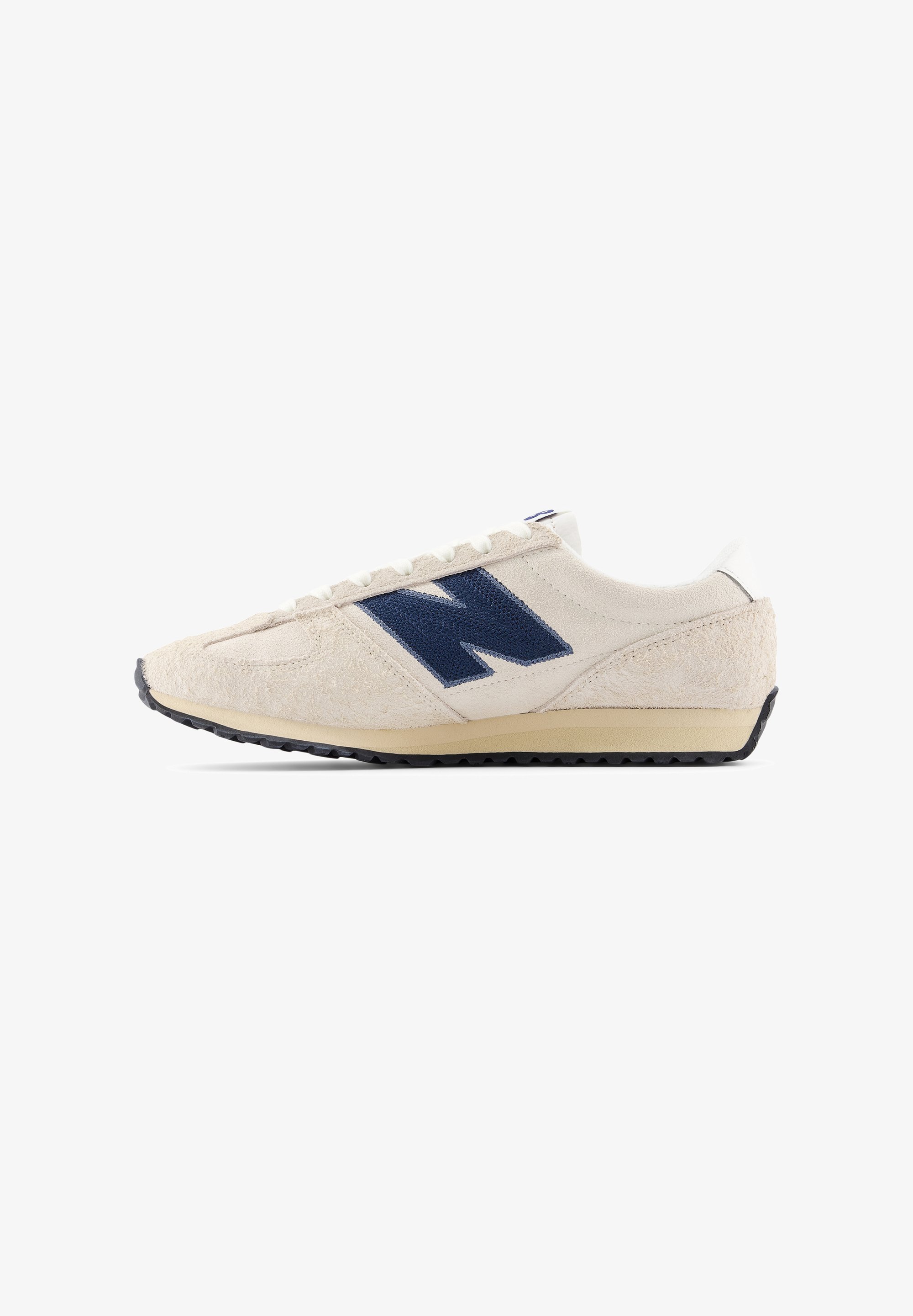 Zapatilla deportiva con parte superior de ante beige, logo azul marino, detalles blancos y suela de goma negra. Cuenta con cordones planos y diseño aerodinámico.