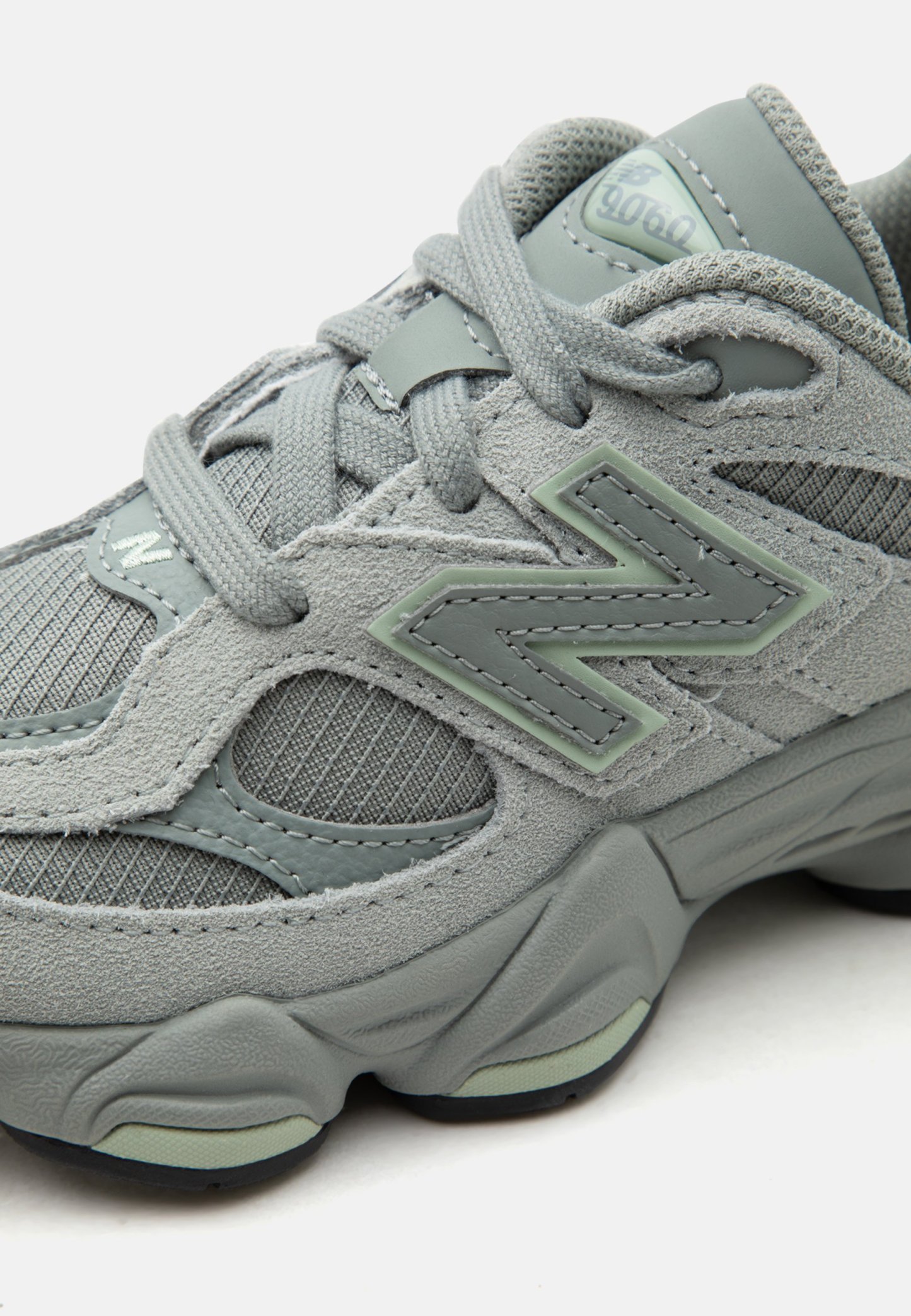Zapatilla gris New Balance 9060 con parte superior de ante y malla, suela gruesa acolchada y cordones grises atados en un lazo.