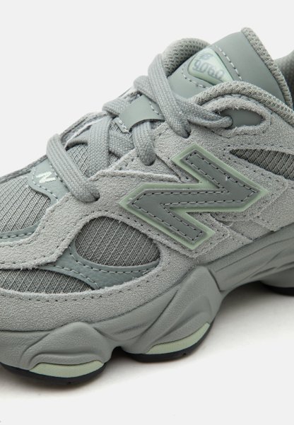 Zapatilla gris New Balance 9060 con parte superior de ante y malla, suela gruesa acolchada y cordones grises atados en un lazo.