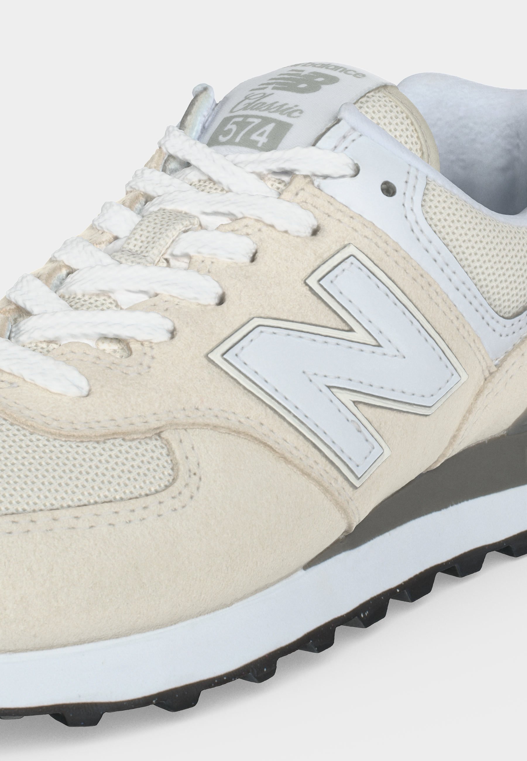 Zapatilla New Balance 574 Classic beige y blanca con cordones blancos, parte superior de malla y ante, y suela negra texturizada.