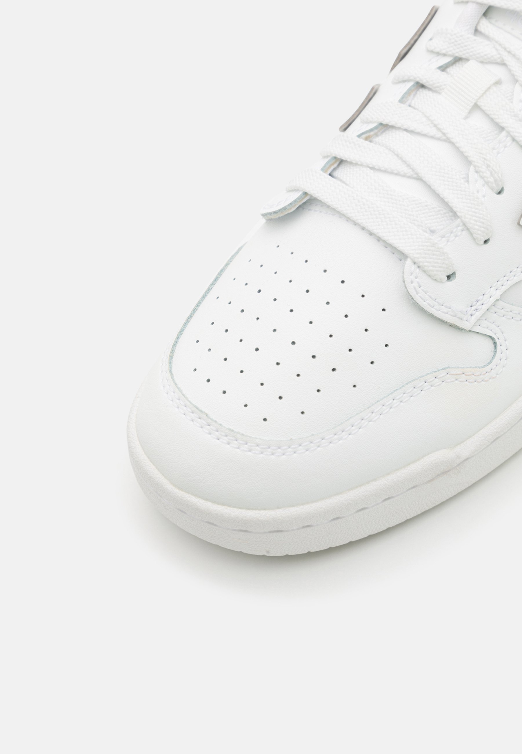 Zapatilla blanca de cuero con caja de dedos perforada, cordones blancos planos y suela de goma de color claro. Diseño redondeado con detalles de costura mínimos.