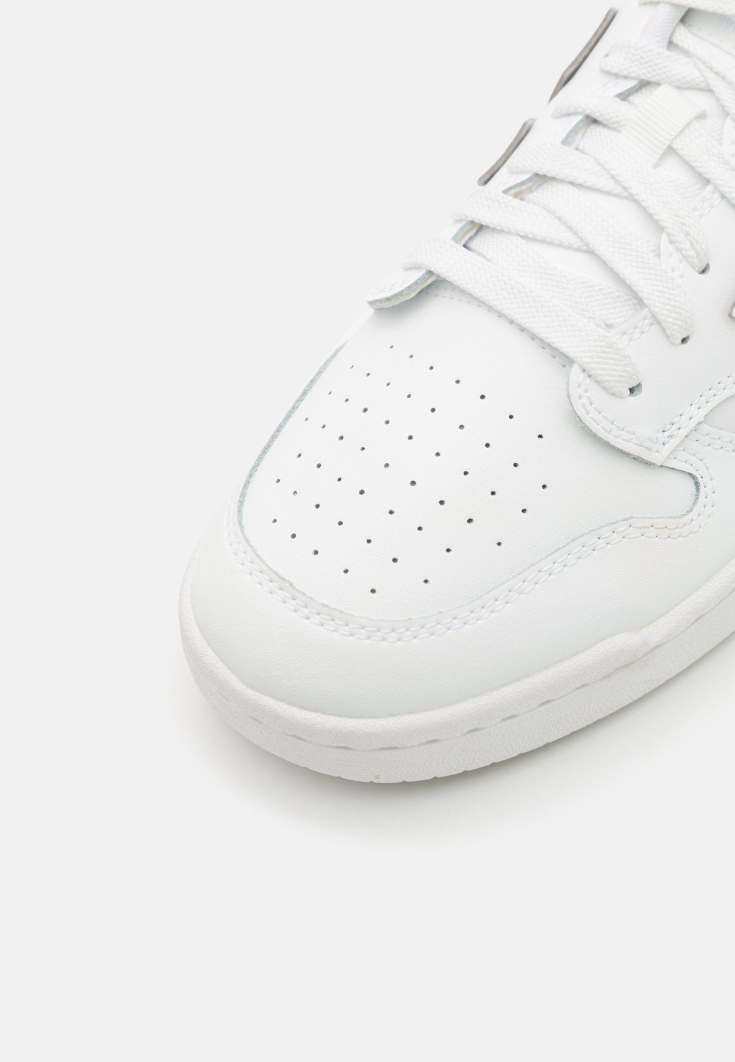 Zapatilla blanca de cuero con caja de dedos perforada, cordones blancos planos y suela de goma de color claro. Diseño redondeado con detalles de costura mínimos.