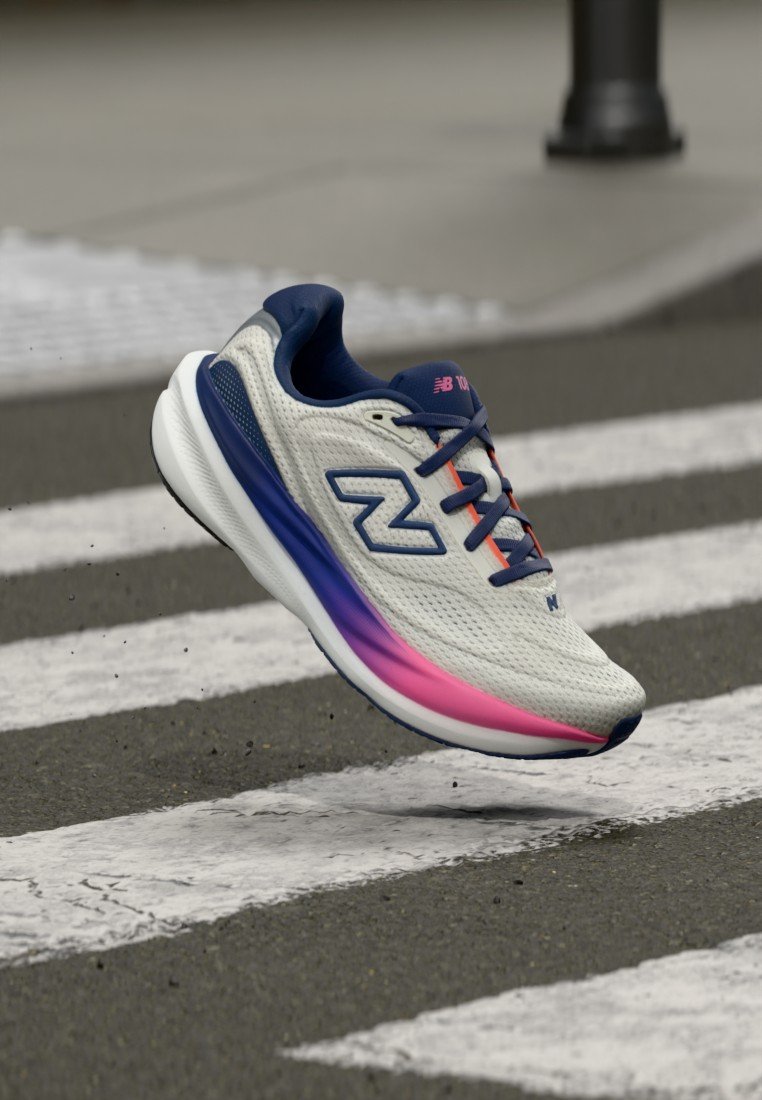 Zapatilla de running New Balance blanca con suela azul y rosa, cordones azul marino, flotando sobre un paso de cebra en asfalto.