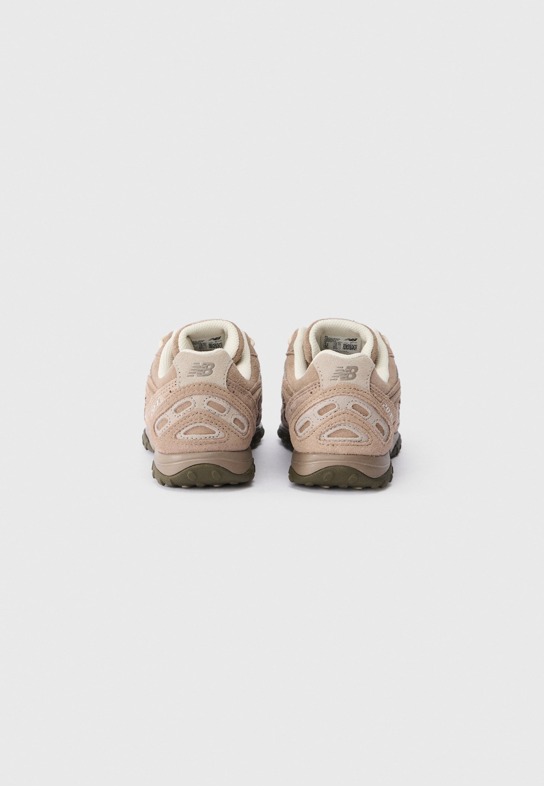 Un par de zapatillas New Balance beige vistas desde atrás, con material de nobuk y suelas de goma oscuras sobre un fondo blanco.