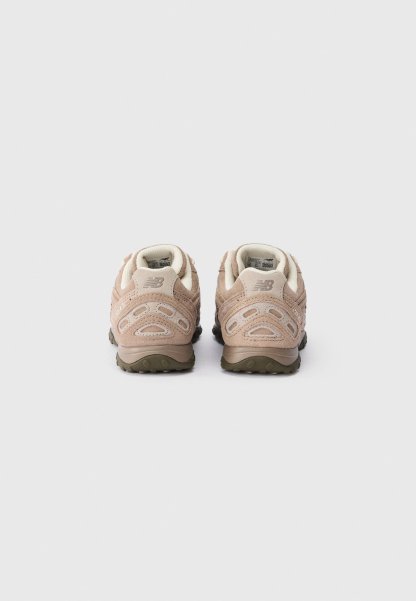 Un par de zapatillas New Balance beige vistas desde atrás, con material de nobuk y suelas de goma oscuras sobre un fondo blanco.