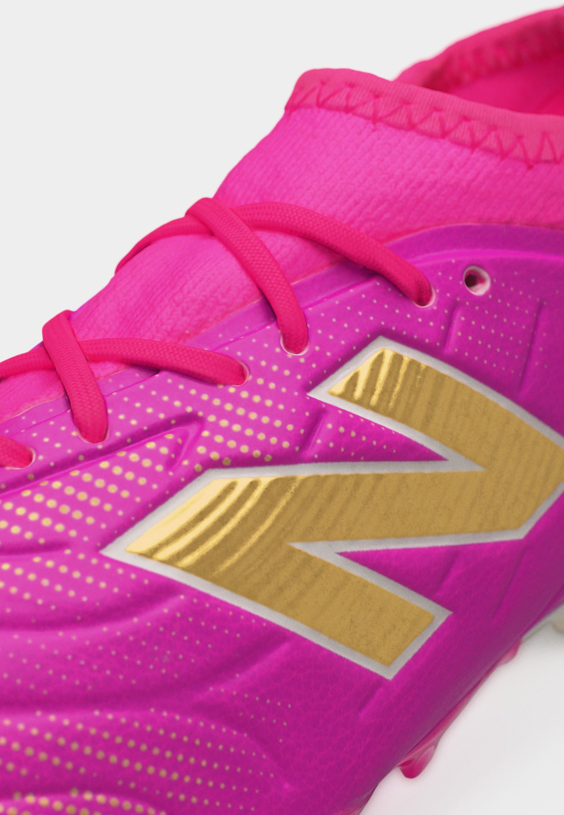 Primer plano de un zapato deportivo rosa con cordones rosas y un gran logo dorado en el lateral, decorado con pequeños puntos dorados.