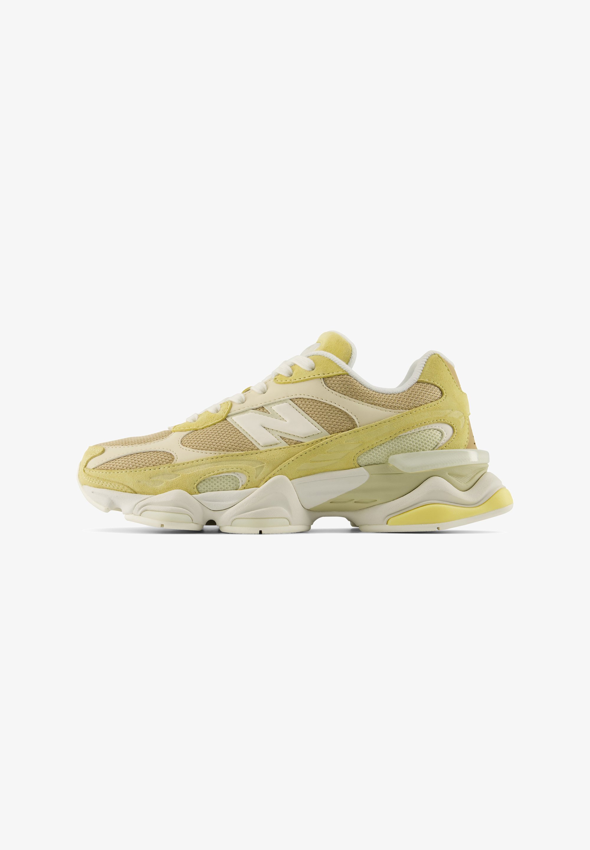 Deportivo New Balance amarillo y beige con cordones blancos, tejido de malla, paneles de ante y suela gruesa y texturizada sobre fondo blanco.